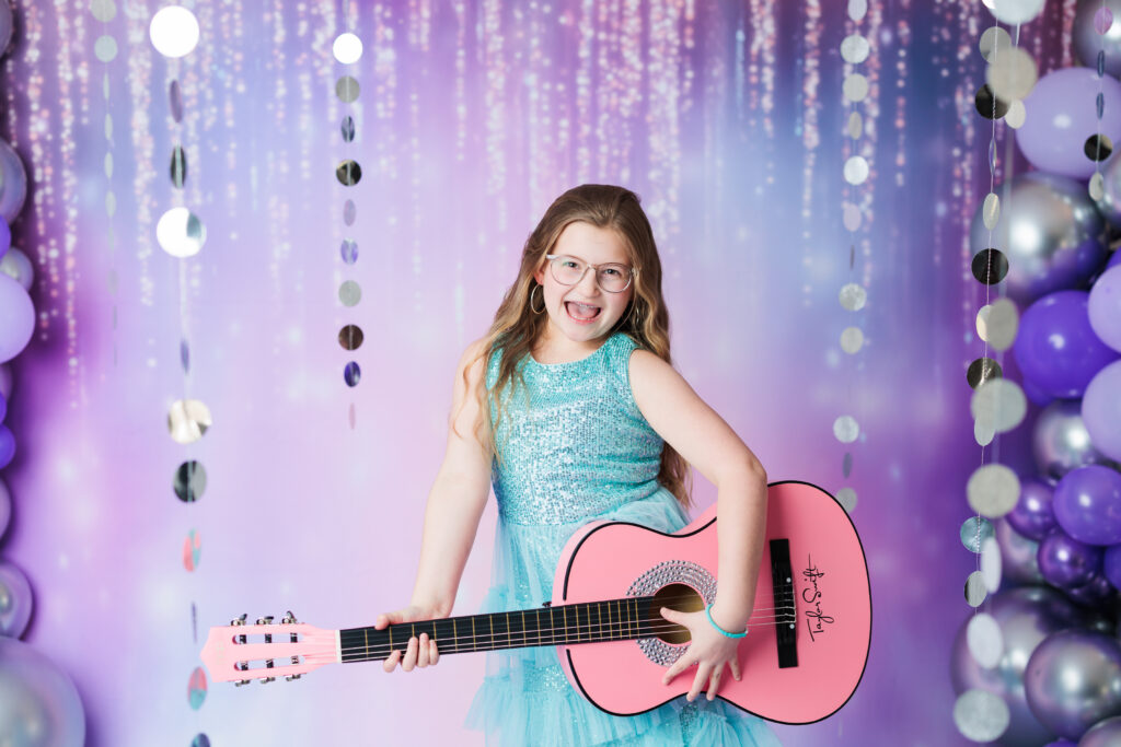 girl in blue dress on pink and purple background playing pink guitar Taylor Swift Photoshoot