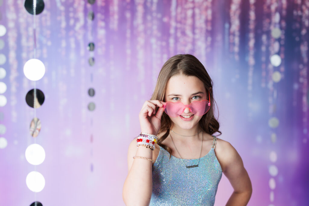 girl holding pink heart glasses on her face wearing friendship bracelets Taylor Swift Photoshoot