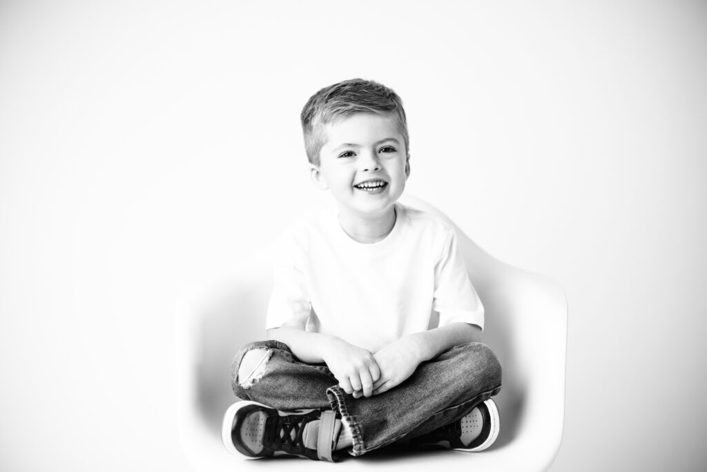 boy sitting in white chair criss cross smiling