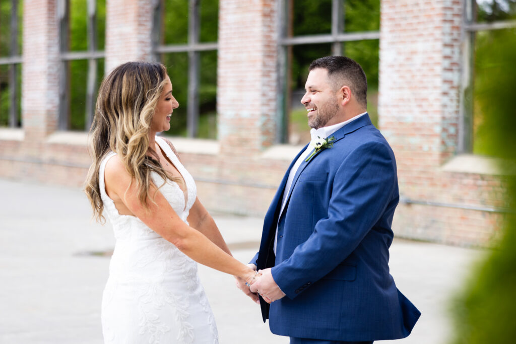bride and groom holding hands laughing facing each other 