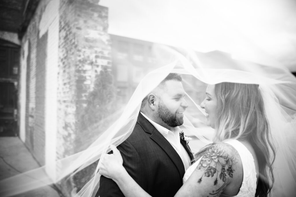 black and white photo of bride and groom looking at each under brides veil 