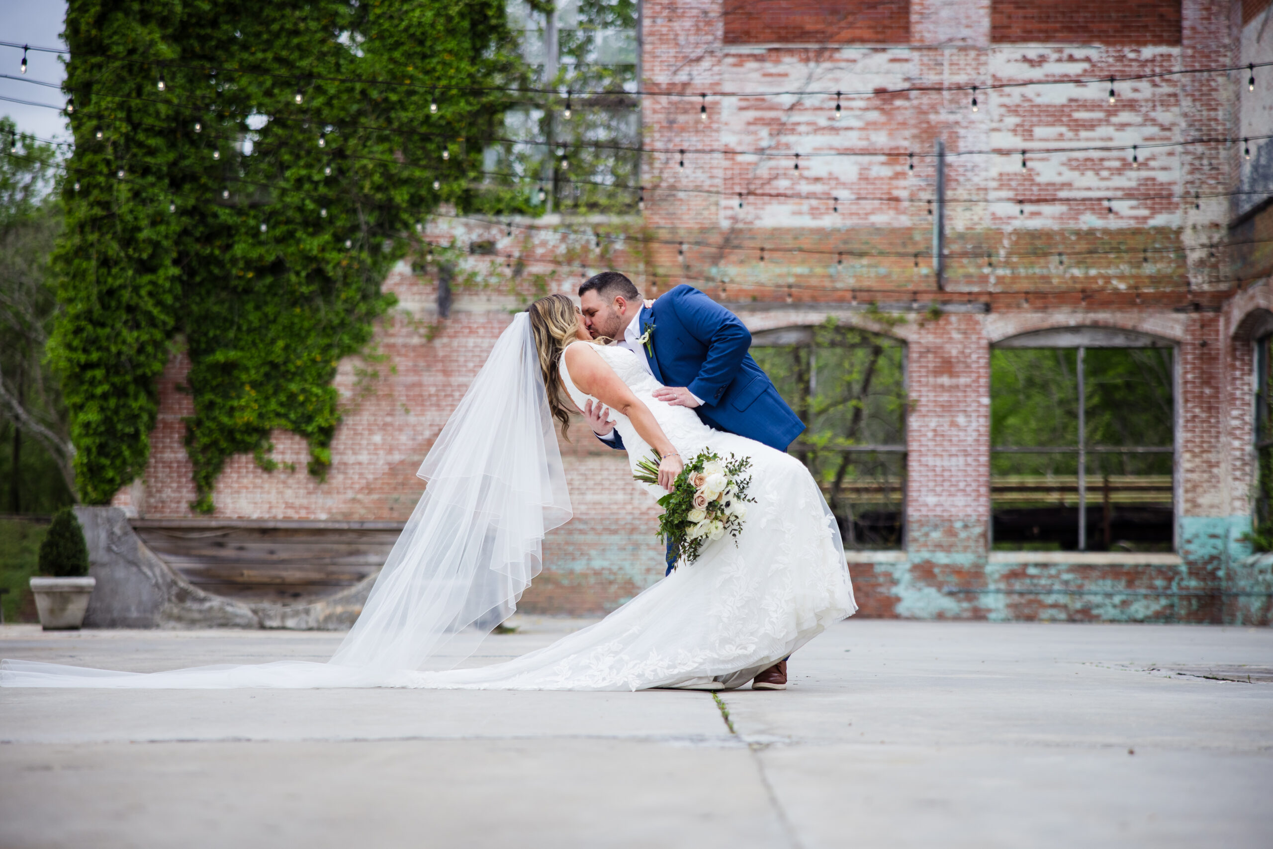 groom dipping and kissing bride with a brick and greenery backdrop