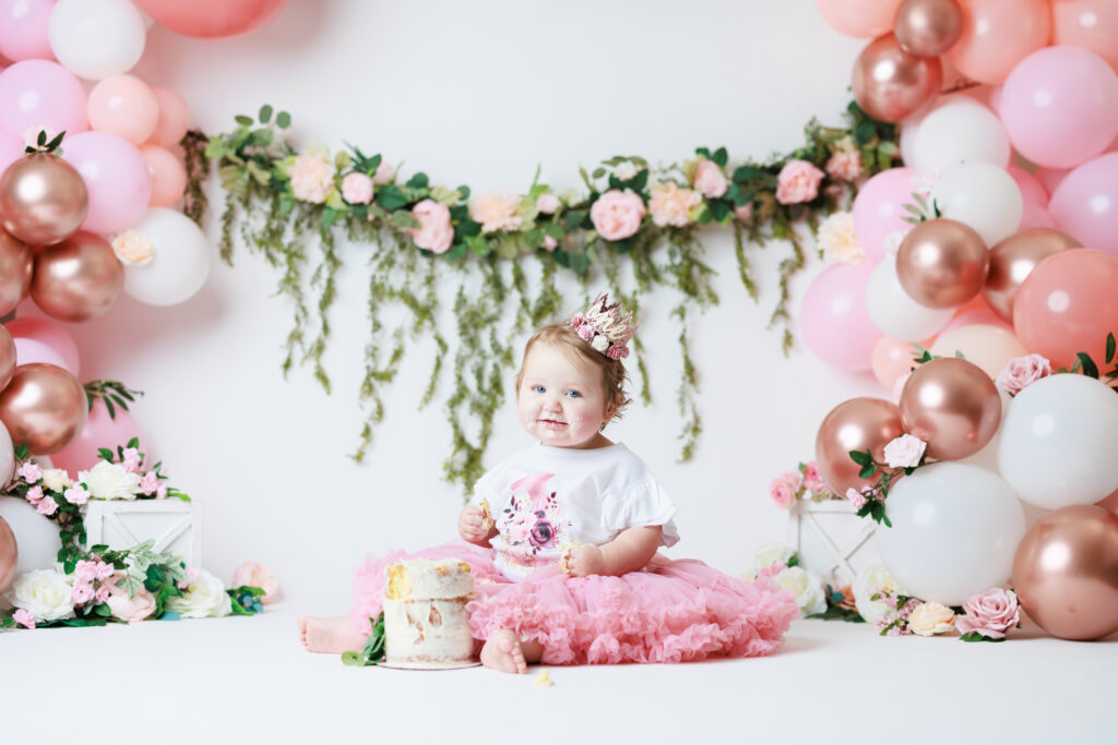 girl sitting with smash cake with flowers and floral garland in background
