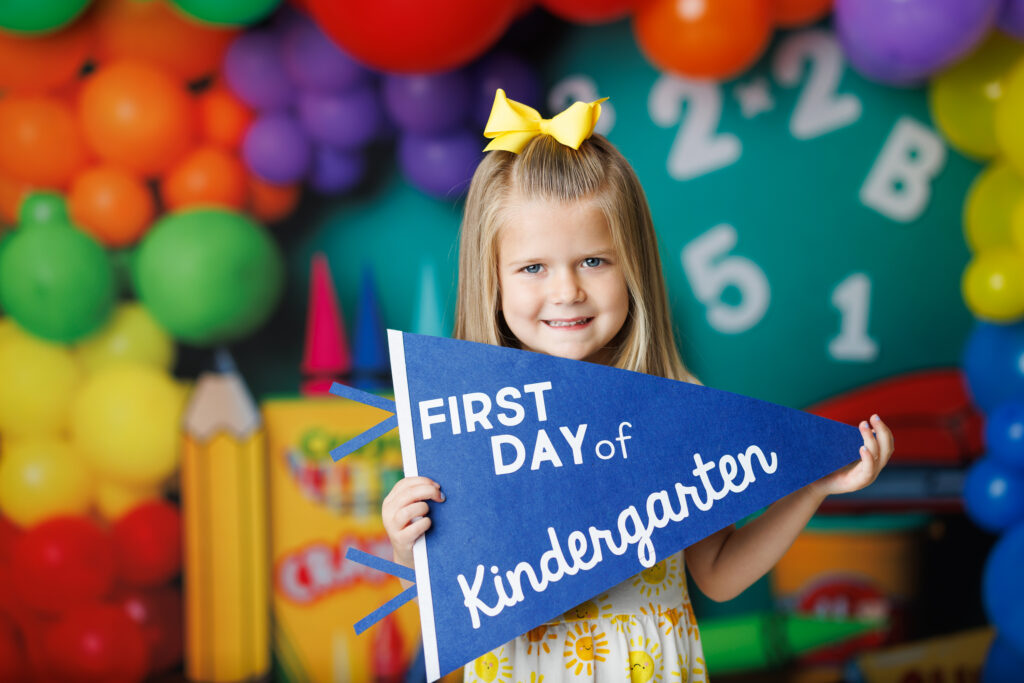 girl holding first day of kindergarten flag with balloons 