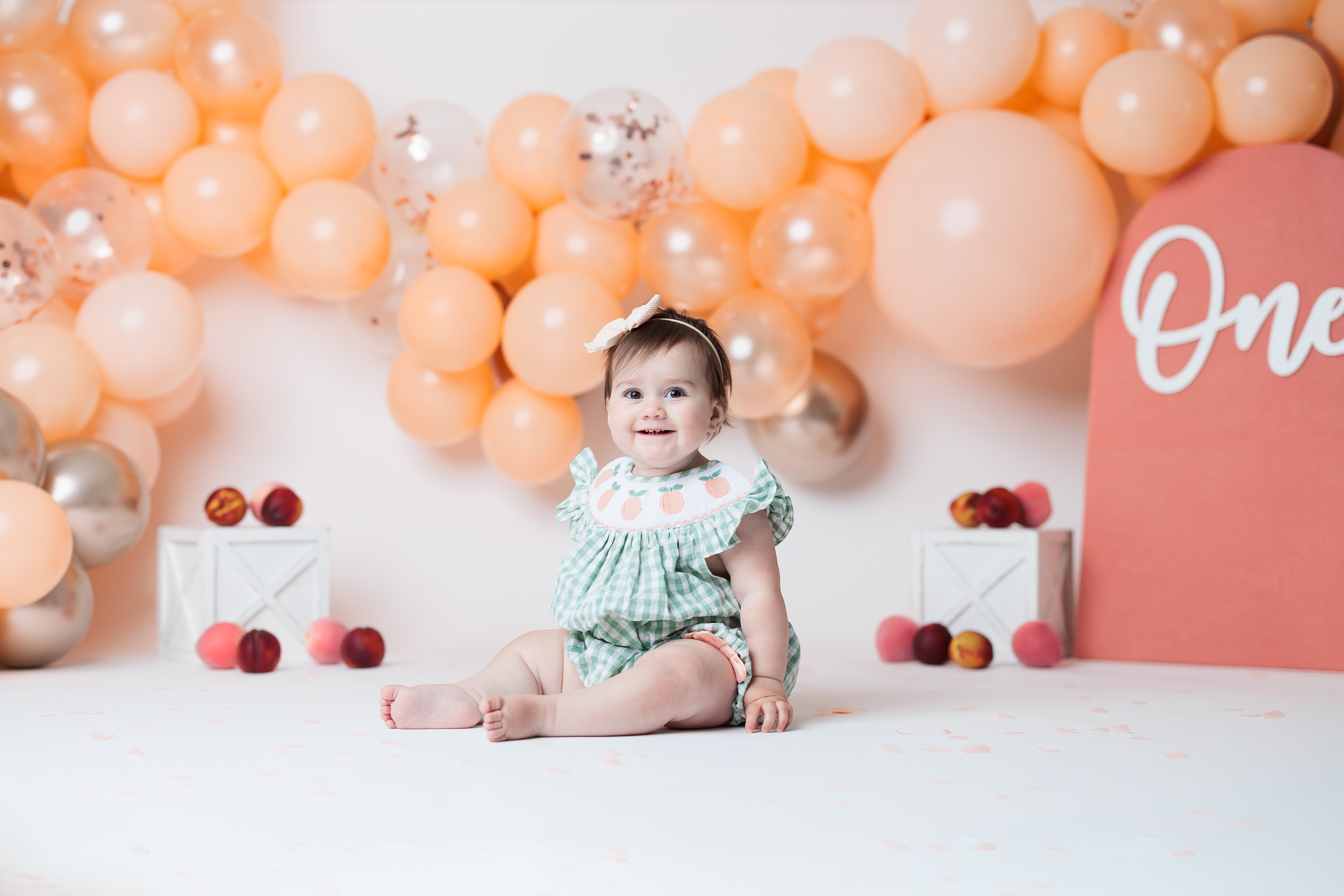 baby sitting in front of peach ballon garland surrounded by peaches