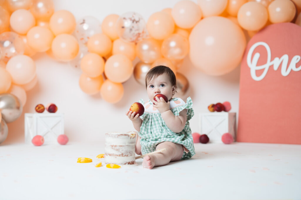 baby eating peaches at a cake smash first birthday session with peach balloons in the background