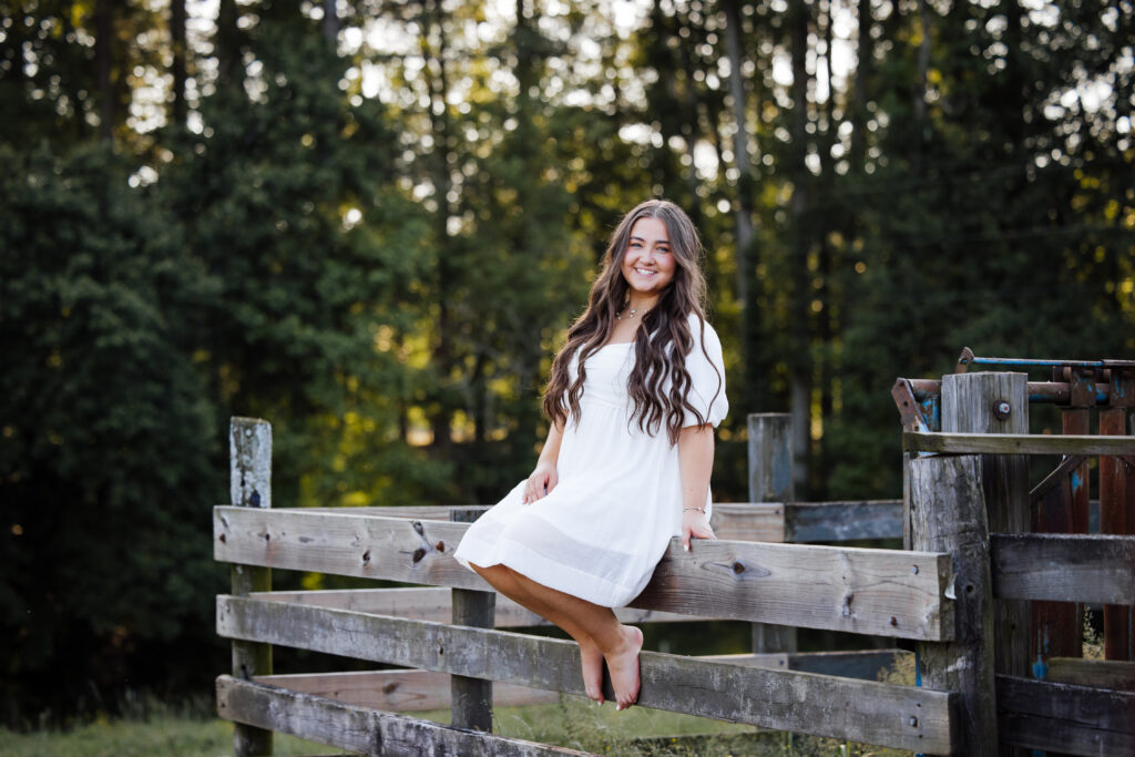 girl sitting on fence in white dress senior graduation session 