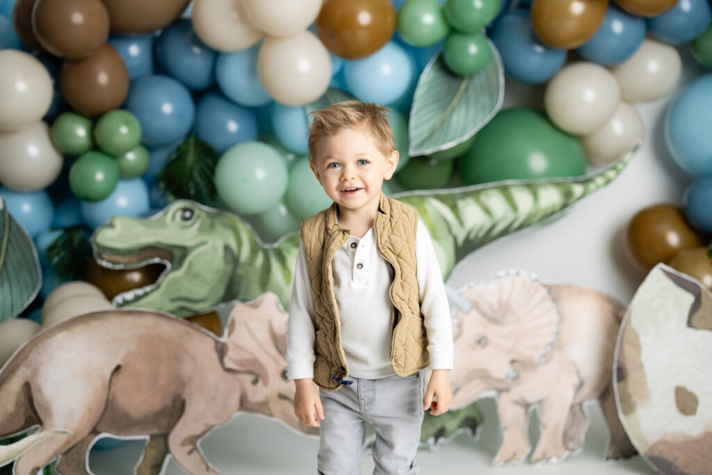 boy smiling in front of blue and green balloon arch with dino decor 