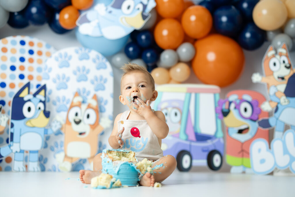 One-year-old laughing while smashing Bluey cake at Victoria Lee Photography studio

