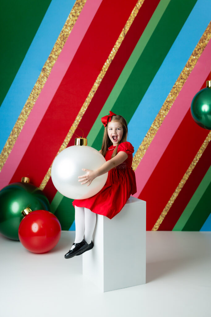 Family and children posing in a colorful Christmas mini-session studio set with oversized ornaments and festive holiday stripes in Canton, GA.