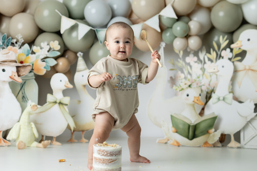 Laughing baby girl with icing on her hands and face surrounded by whimsical goose decorations

