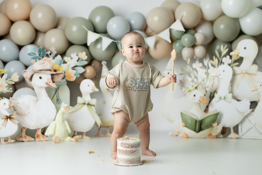 Baby girl holding a wooden spoon and giggling during her first birthday cake smash session