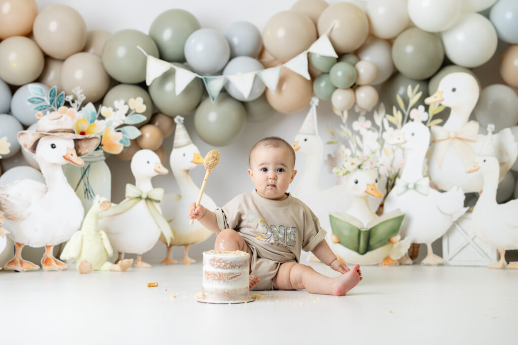One-year-old girl sitting in a One Silly Goose themed cake smash set with handmade neutral-toned props in Canton, GA