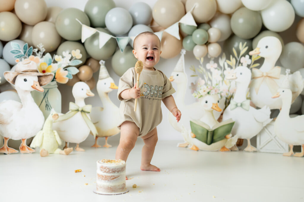 Baby girl holding a wooden spoon and giggling during her first birthday cake smash session