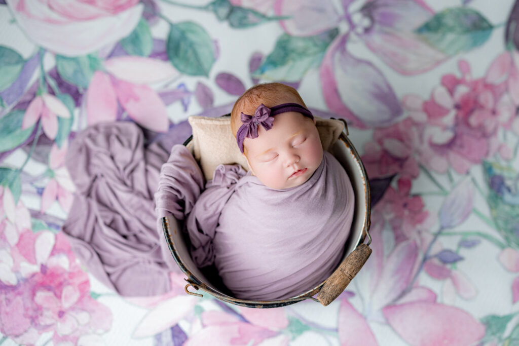 Newborn redhead baby girl in soft purple wrap with delicate headband.