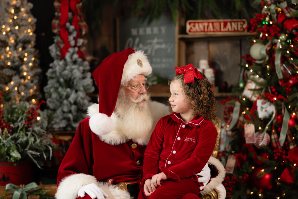 Santa mini session in Canton GA studio with young girl wearing red Christmas pajamas