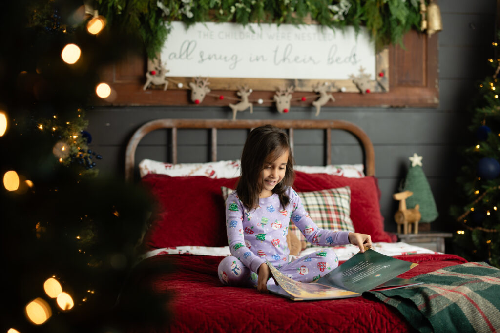 Little girl reading Christmas storybook during pajama mini session in Canton GA studio