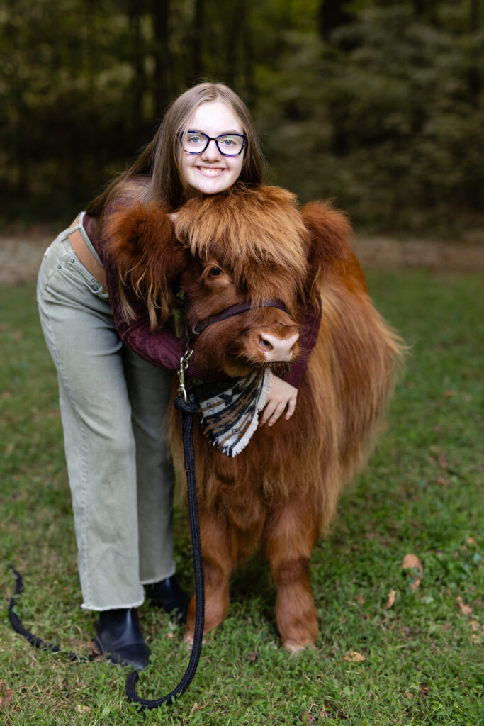 Children smiling with a fluffy highland cow during mini session
