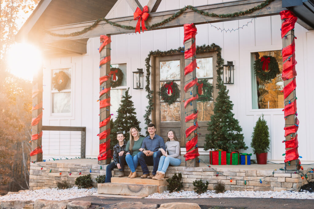 Family sitting on decorated front porch with Christmas wreaths and lights.