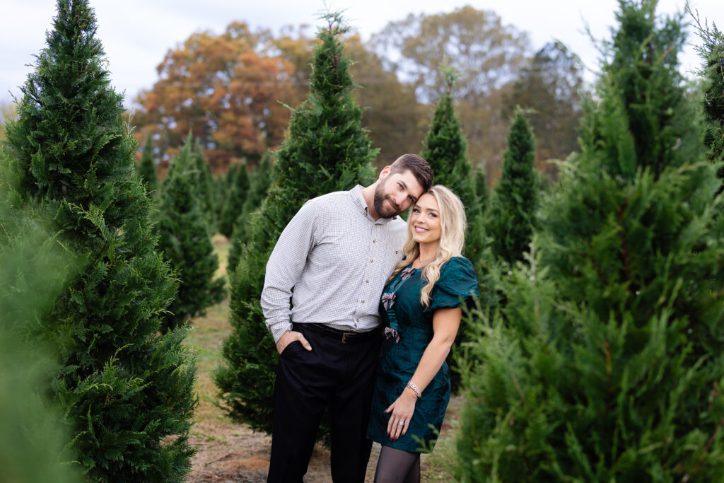 Couple embracing between evergreen trees at Christmas tree farm.