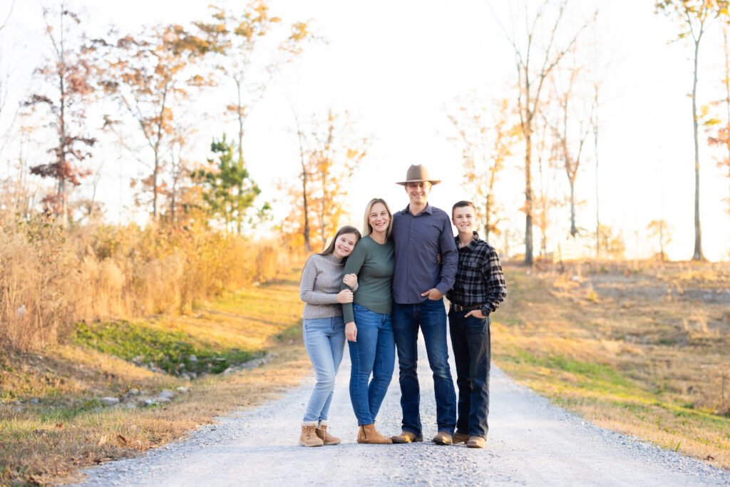 Family standing on gravel driveway with golden trees in background.