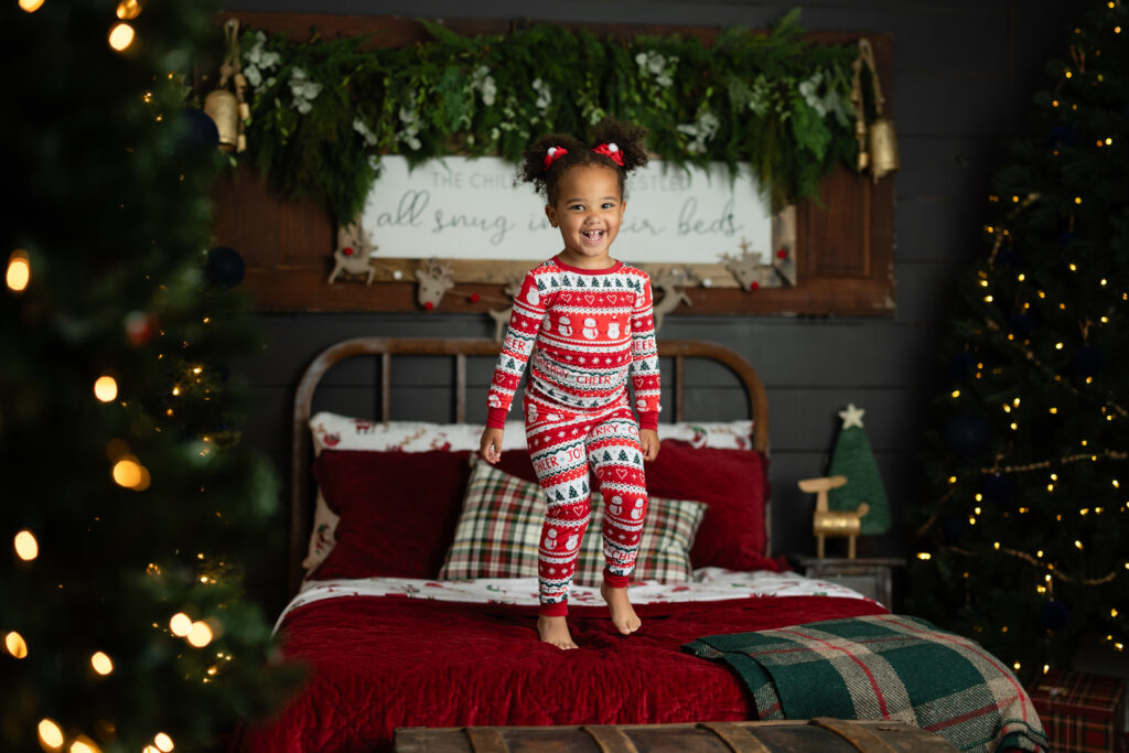 Little girl smiling on cozy Christmas bed in red pajamas.