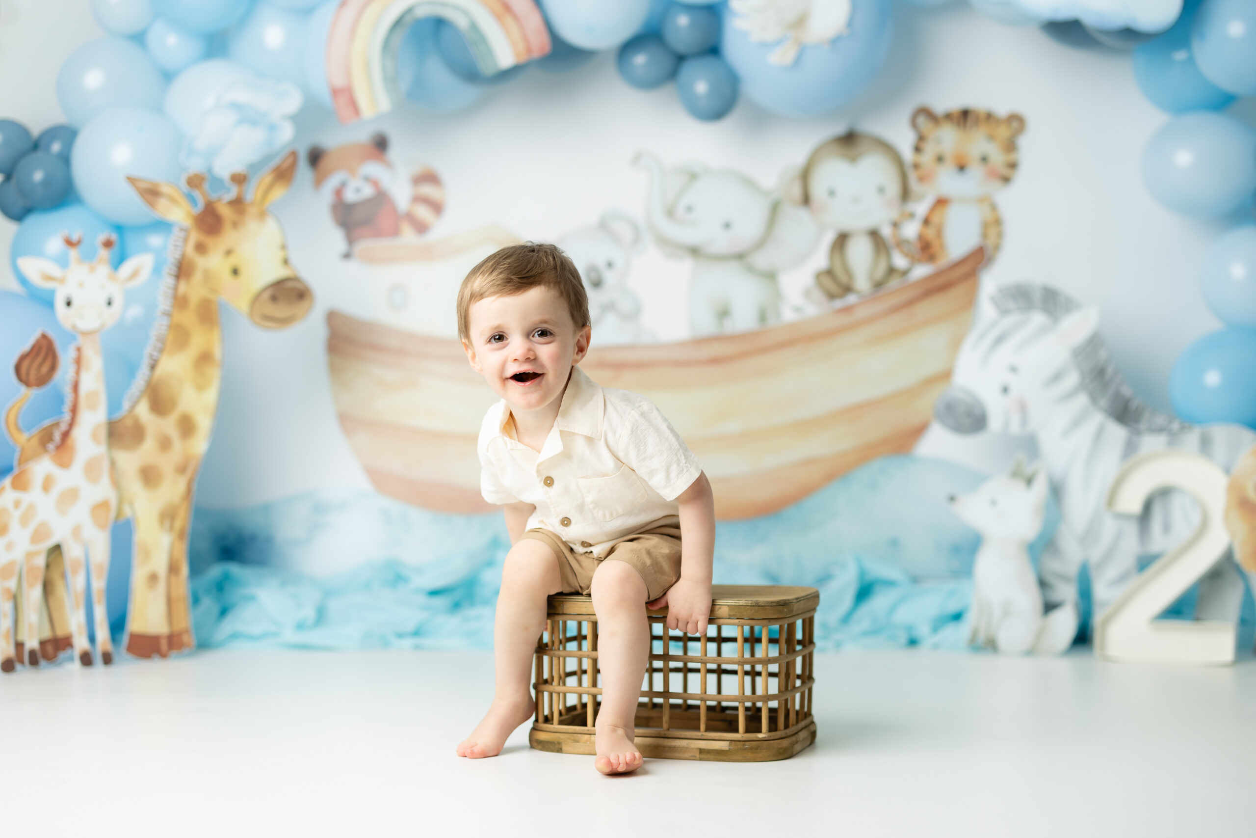 little boy sitting on crate in front of noahs ark themed backdrop