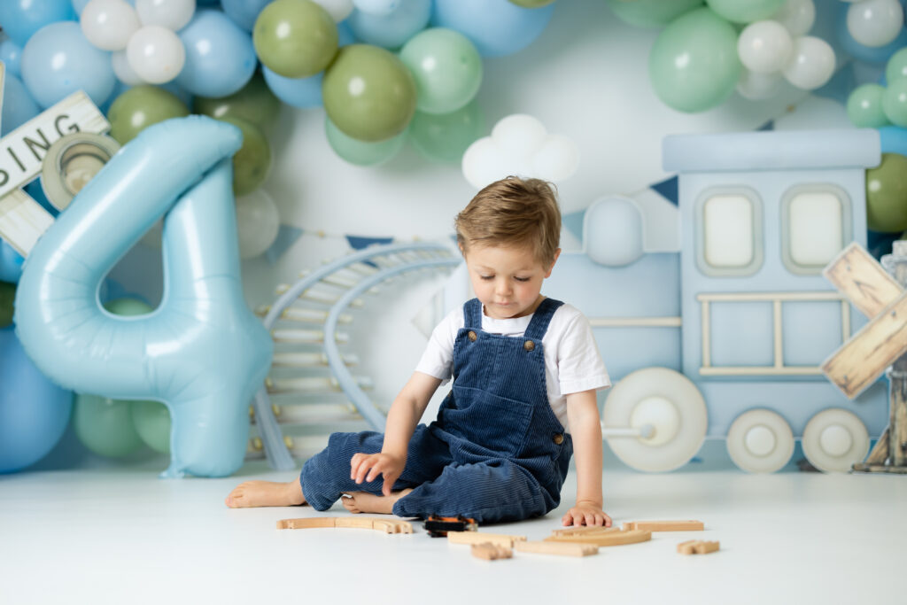 Little boy playing with wooden trains during birthday photography session