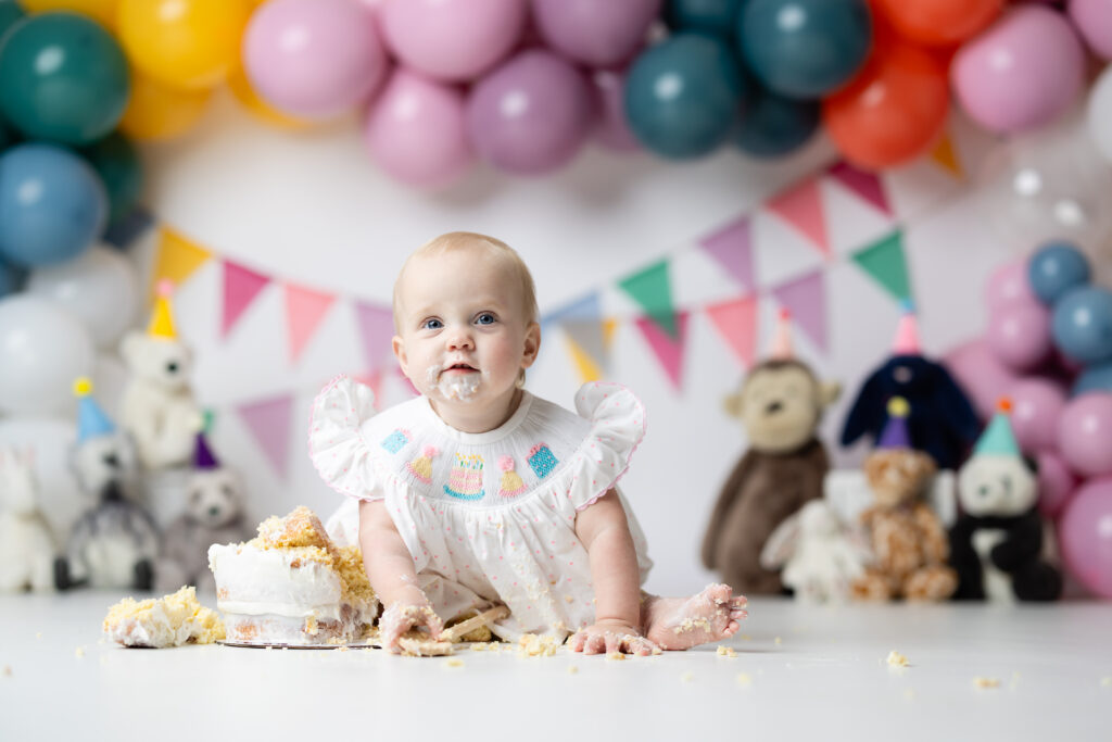 Happy one-year-old holding a wooden spoon during her messy cake smash