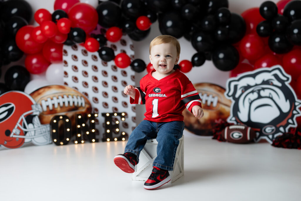 child smiling in a red UGA jersey during his Georgia Bulldogs cake smash session